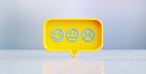 Yellow speech bubble with blue face emojis sitting on before silver defocused background. Horizontal composition with copy space.